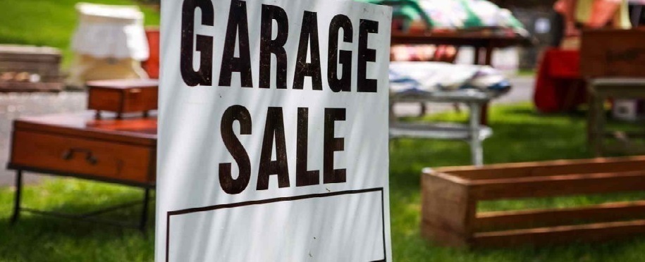 close up of a black and white garage sale sign in front of items set out in a yard for sale