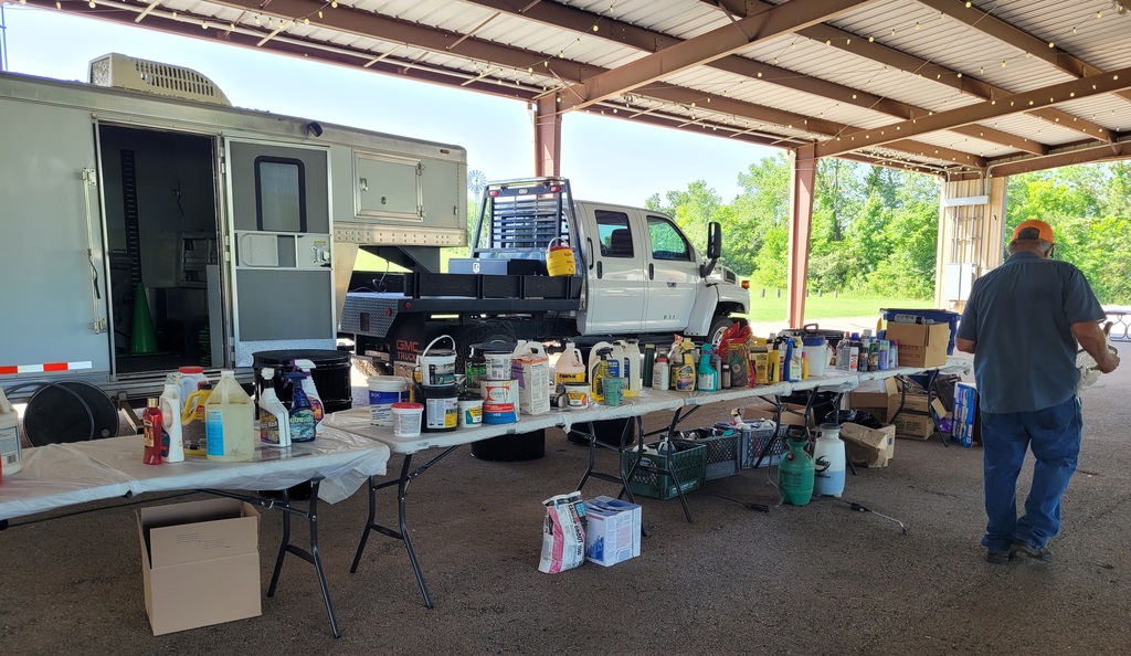 tables with collected household hazardous waste in front of a truck and trailer and a man walking away